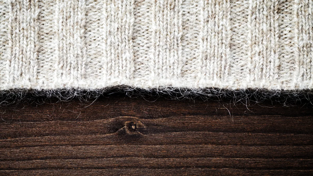A raw wool fleece resting on a rustic wooden table in soft daylight.