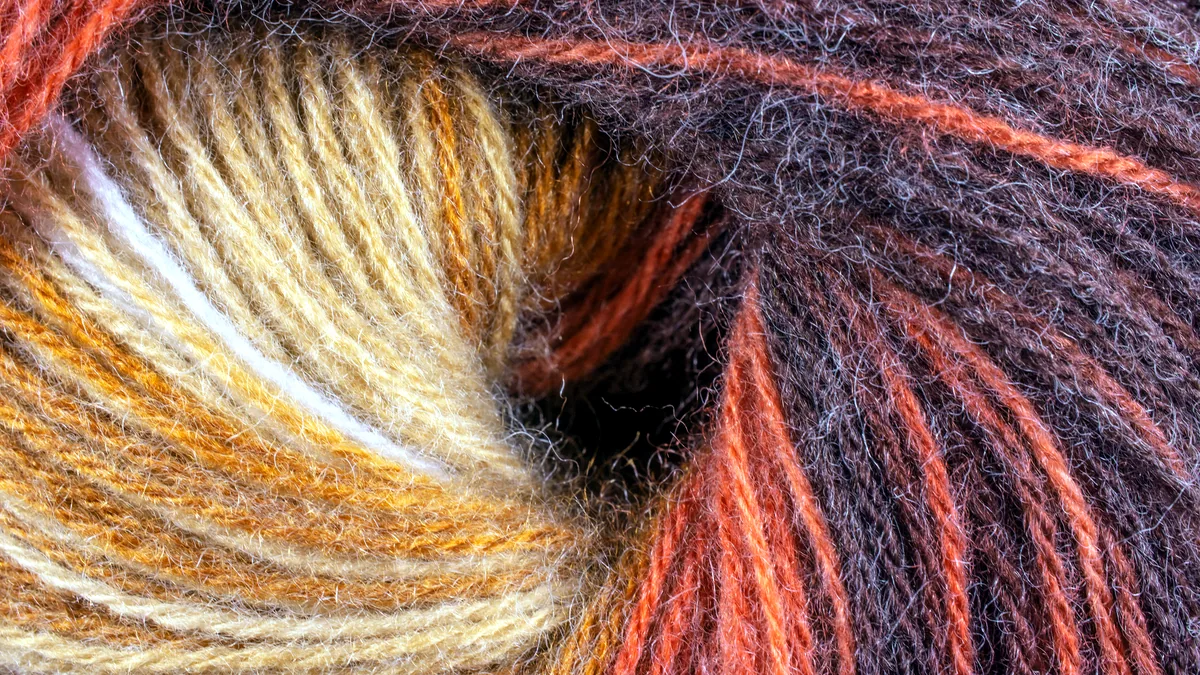 Fine merino wool strands in pale cream tones, held in soft daylight.